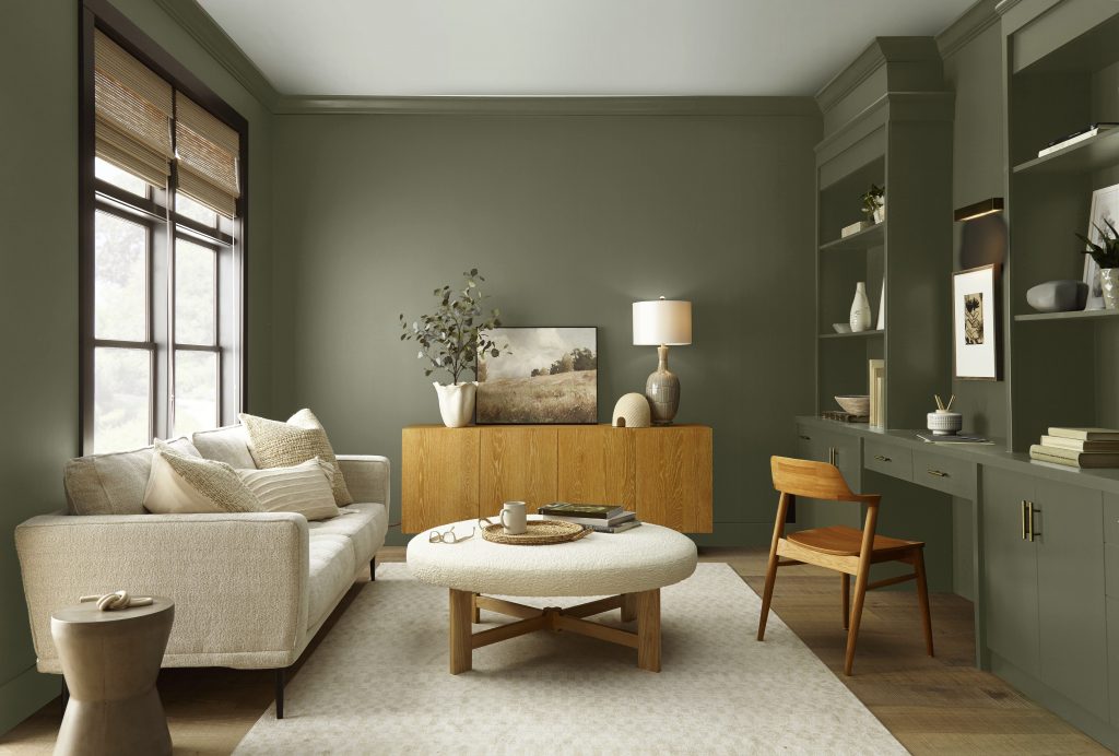 Casual living room with a warm dark green painted walls and built-ins, featuring a hidden desk area, sofa, coffee table, wood cabinet, and soft natural light.