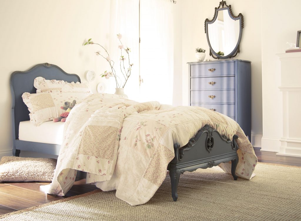 Bedroom with Polished Pearl cream wall paint, vintage-style bed, soft layered bedding, muted blue furniture accents, and natural light for romantic bedroom color inspiration.