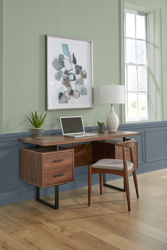 Home office pairing BEHR Bitter Sage N390-4 sage green walls with Midnight Blue N480-7 wainscoting and a wood desk.