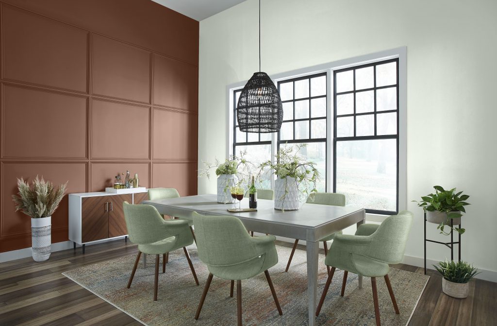 Dining room with BEHR Earth Fired Red S200-7 and Unwind GR-W05 walls, sage green chairs and a wood dining table.