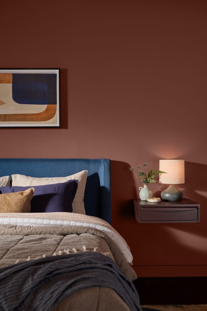 Bedroom with walls painted Tuscan Terra T27-02, a warm clay-toned color paired with blue, gray, and neutral bedding, natural wood, and soft lighting.
