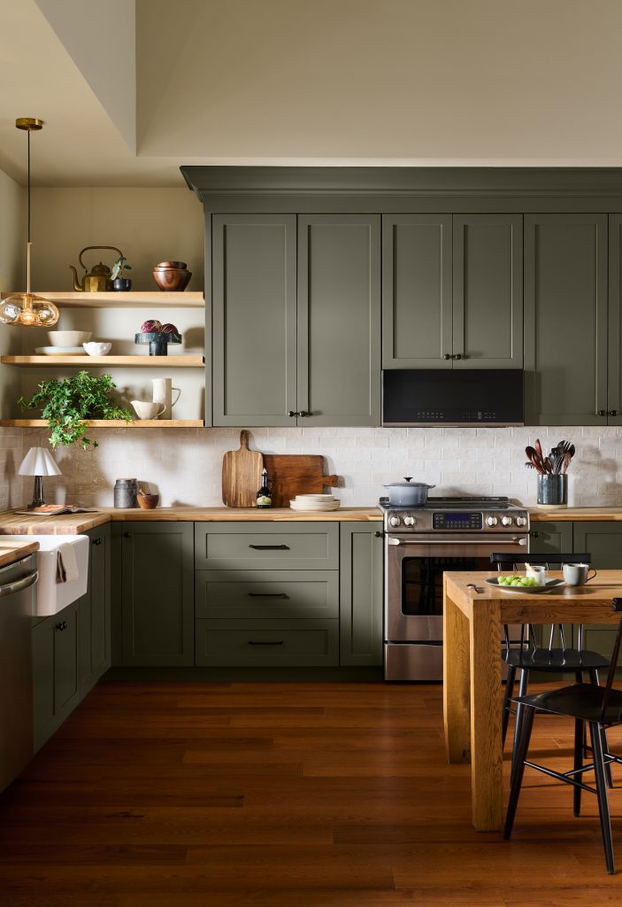 A welcoming kitchen with cabinets painted in BEHR Grounded T27-01, featuring warm wood countertops, open shelving, stainless steel appliances, and a round dining table.