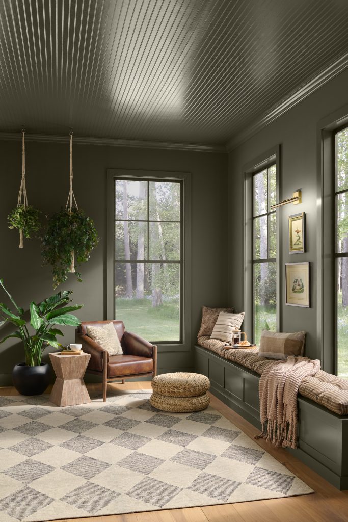 Sunroom with walls and paneled ceiling painted Grounded T27-01, a mossy olive green with earthy brown undertones, paired with natural wood, woven textures, and greenery.