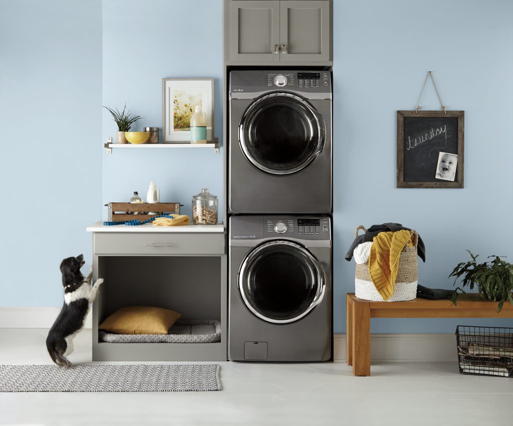 Laundry room with walls painted Denim Light PPU14-15, a soft sky-inspired blue paired with dark cabinetry, white surfaces, warm wood, and woven accents.