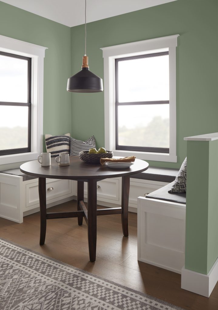 Breakfast nook with BEHR Bitter Sage N390-4 sage green walls, white built-in benches and a round wood table.