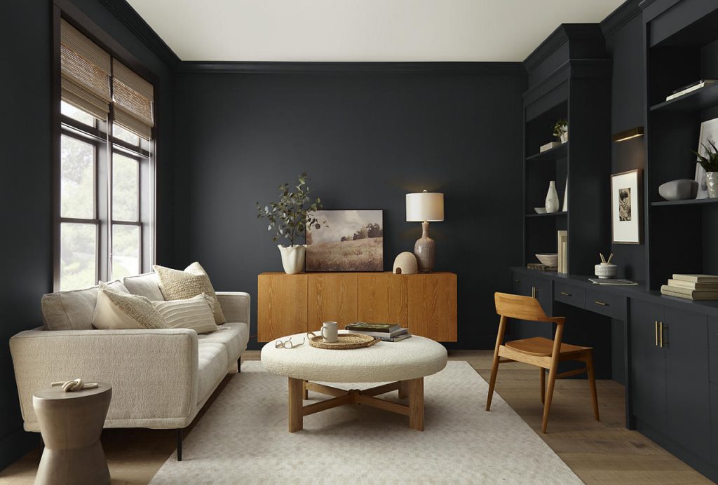 A moody modern living room with walls, trim, built-in desk, and cabinetry painted Cracked Pepper, a soft black that creates a rich, enveloping backdrop. Light neutral seating, warm wood furniture, woven textures, and natural light soften the dark palette, while the built-ins and streamlined furnishings give the space a refined, contemporary feel.