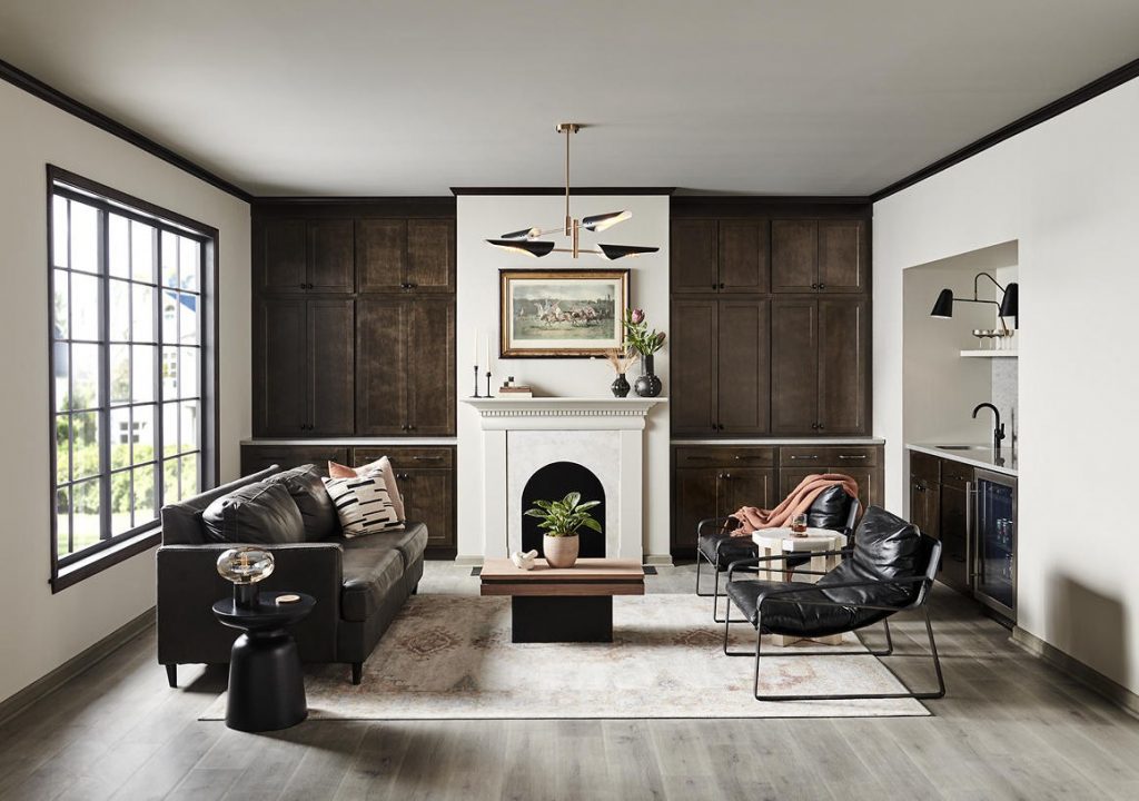A sophisticated contemporary living room with walls painted Tranquil Gray and trim painted BLACK. Dark wood built-ins, black leather seating, a white fireplace, black-framed windows, and warm wood accents create a tailored, high-contrast look. Soft natural light and a muted neutral palette keep the space feeling balanced, polished, and inviting.