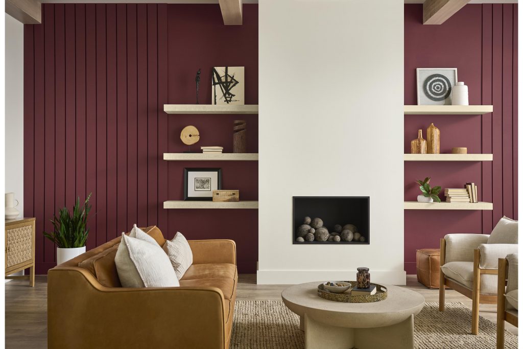 A living room featuring BEHR® Rumors, a rich ruby red, on vertical paneled accent walls, paired with a Blank Canvas fireplace, warm wood furnishings and neutral seating.