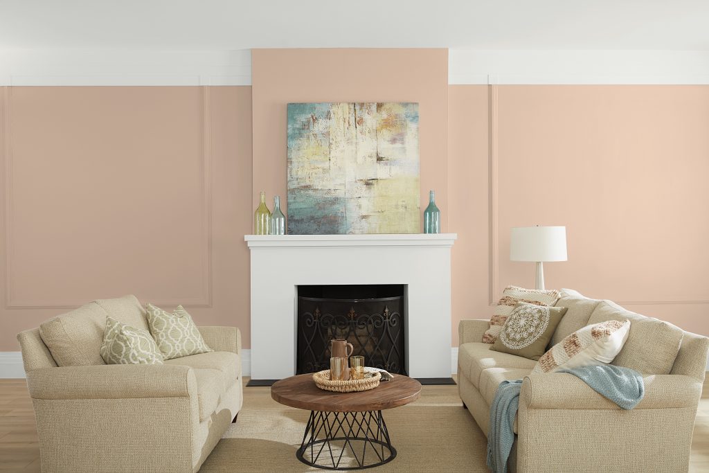 A living room featuring a subdued peach wall color called Mesquite Powder with crisp white trim and fireplace, complemented by soft neutral seating, warm wood accents, and light blue decorative touches for an airy, inviting feel.