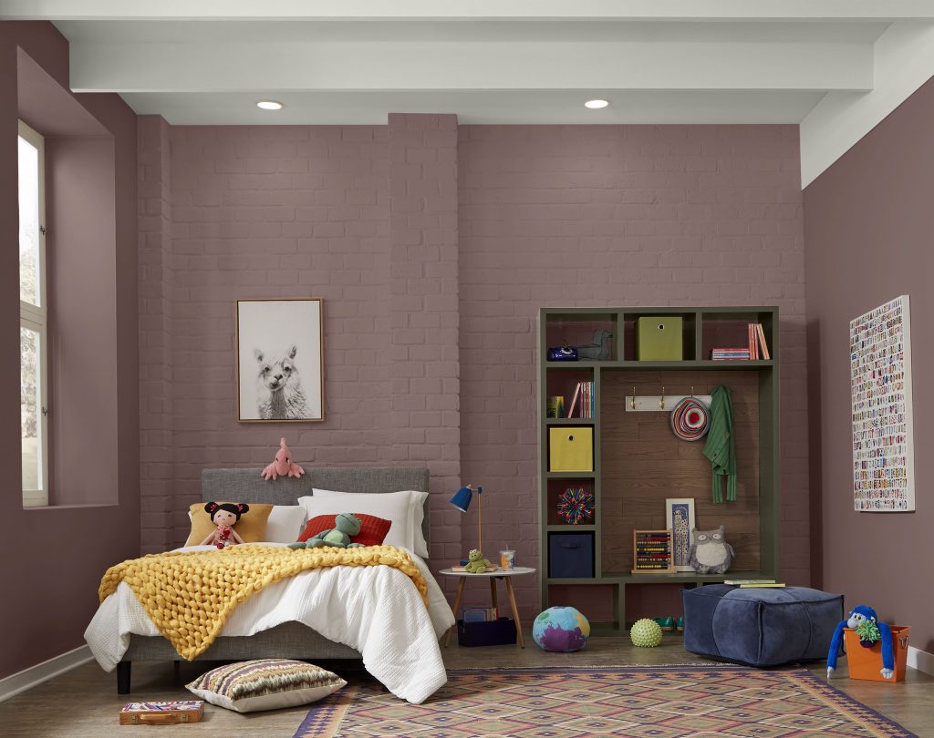 A spacious kids’ room with walls painted BEHR Smokey Claret, Polar Bear trim, and Grounded on the shelving. White-painted brick, high ceilings, playful toys, layered textiles, and colorful accents.