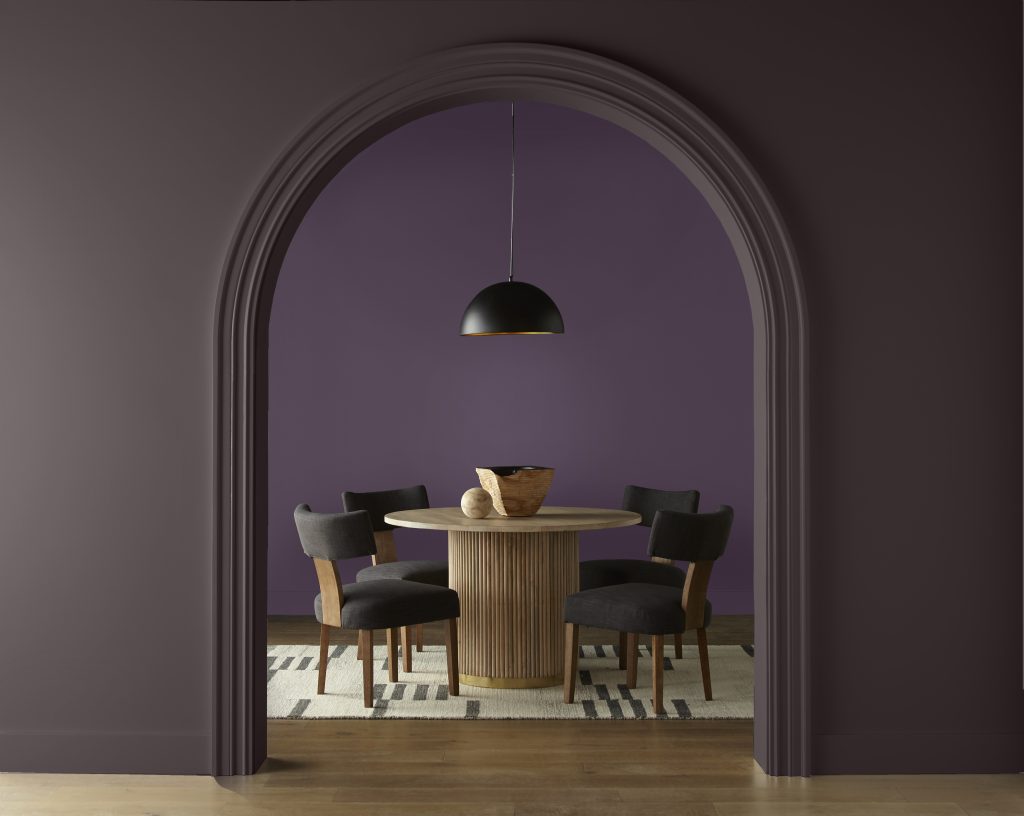 Dining room with Deep Merlot M100-7 walls revealed through an arched opening framed by Sarsaparilla HDC-AC-26, with a round wood table, dark chairs and black pendant light.