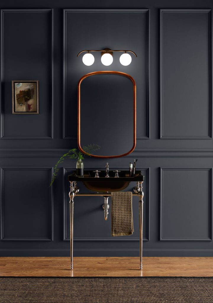 Bathroom with paneled walls painted Nightfall T27-04, paired with a dark console sink, warm metallic mirror and fixtures, wood flooring and black accents.