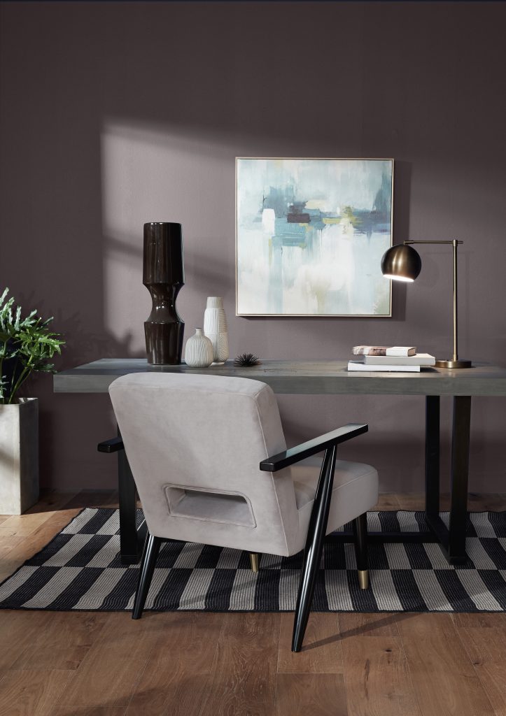 Home office with walls painted Sarsaparilla HDC-AC-26, styled with a dark wood desk, cream upholstered chair, abstract artwork, greenery and warm metallic lighting.