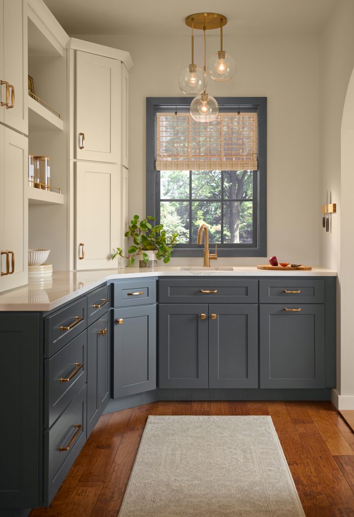 Kitchen with walls painted Lunaria M280-2 and lower cabinets painted Nightfall T27-04, accented by warm wood flooring, brass hardware and natural light.