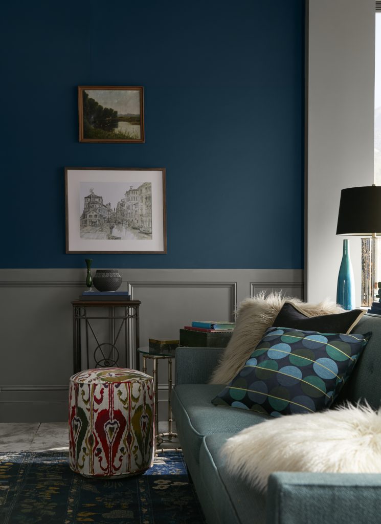 Living room with upper walls painted Nocturne Blue HDC-CL-28 above gray paneled wainscoting, paired with teal seating, patterned textiles and warm wood accents.
