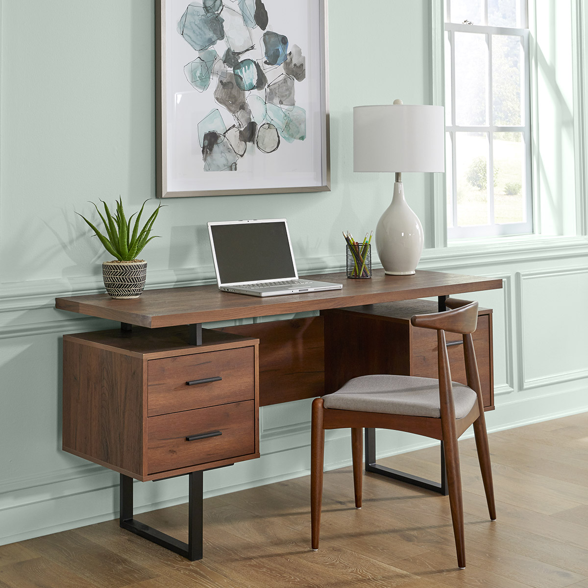 An office space with a wood desk and large piece of art. The walls painted in a soft sea glass green hue.