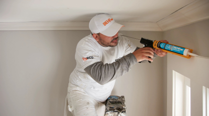Painting professional wearing Behr Pro gear caulking an interior surface